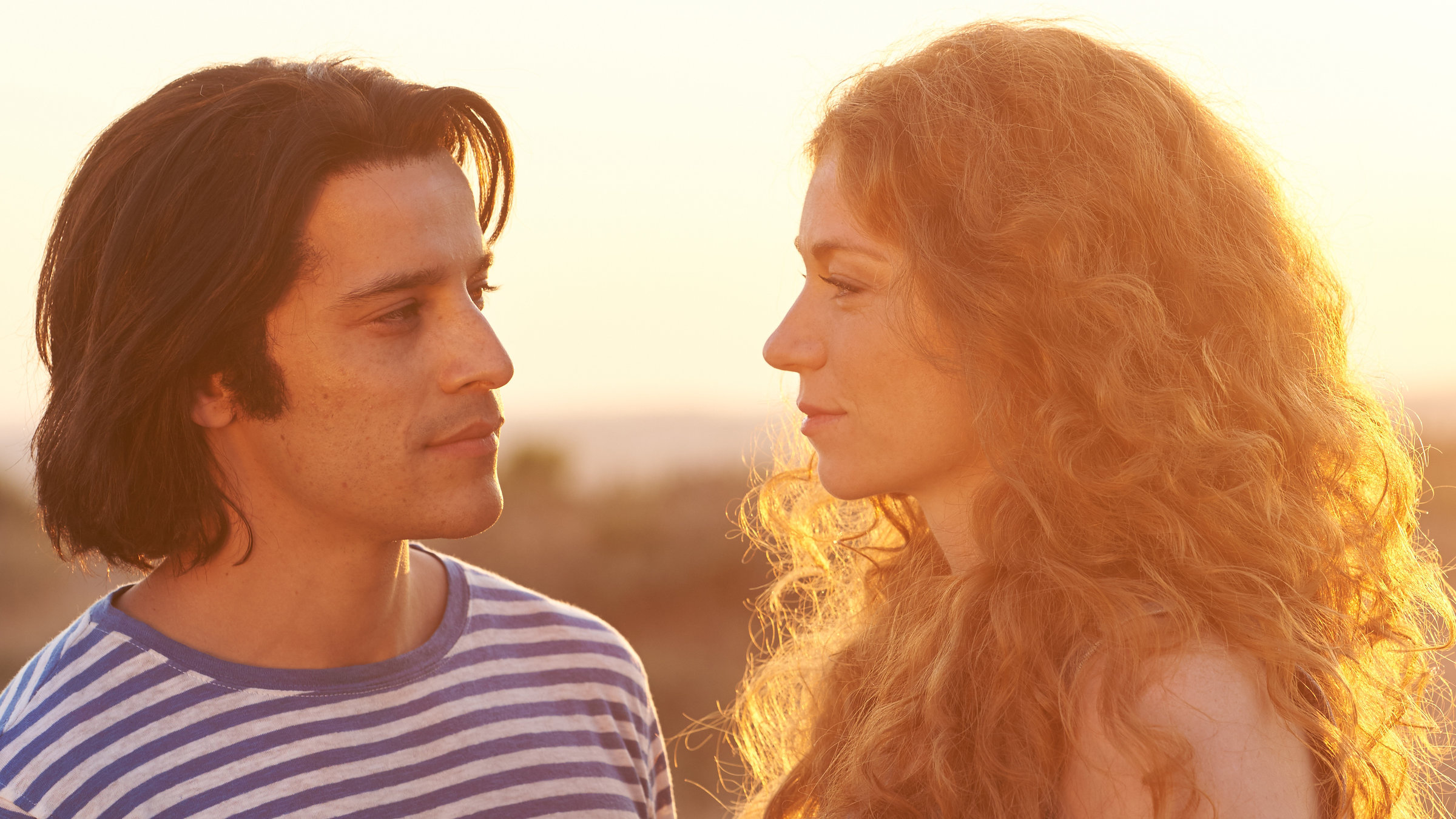 "Bella Germania - Il segreto - Das Geheimnis": Im Sonnenuntergang am sizilianischen Dünenstrand steht der junge Italiener Vincenzo (Kostja Ullmann) neben Tanja (Marleen Lohse), einer politisch sehr aktiven Studentin. Beide schauen entschlossen und ernst.