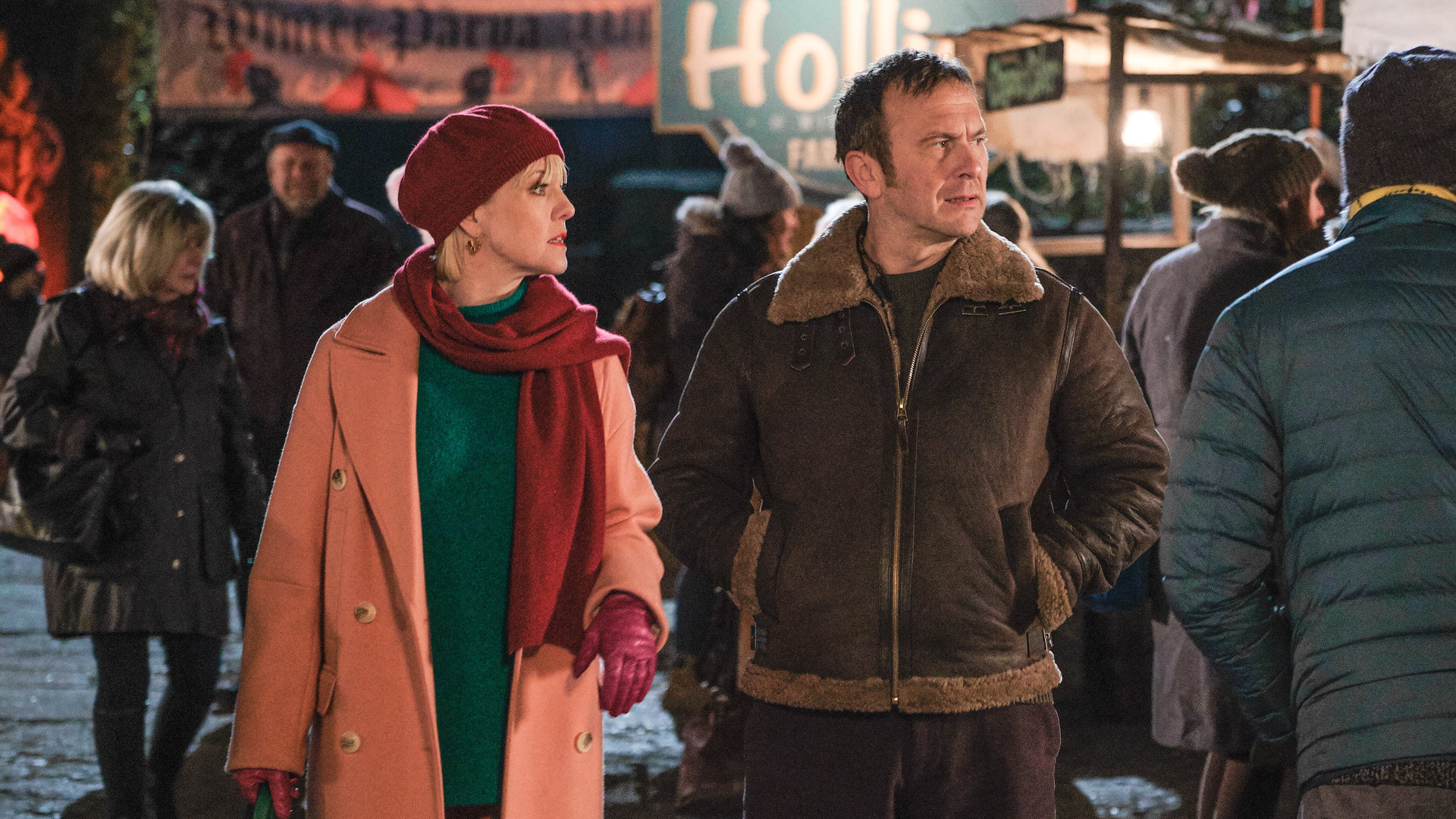 "Agatha Raisin – Und der tote Polizist Teil 1": Agatha Raisin (Ashley Jensen) und Charles Fraiths (Jason Merrels) laufen abends zwischen verschiedenen Ständen des Fests entlang.