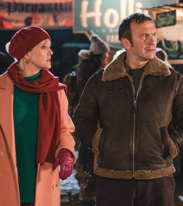 "Agatha Raisin – Und der tote Polizist Teil 1": Agatha Raisin (Ashley Jensen) und Charles Fraiths (Jason Merrels) laufen abends zwischen verschiedenen Ständen des Fests entlang.