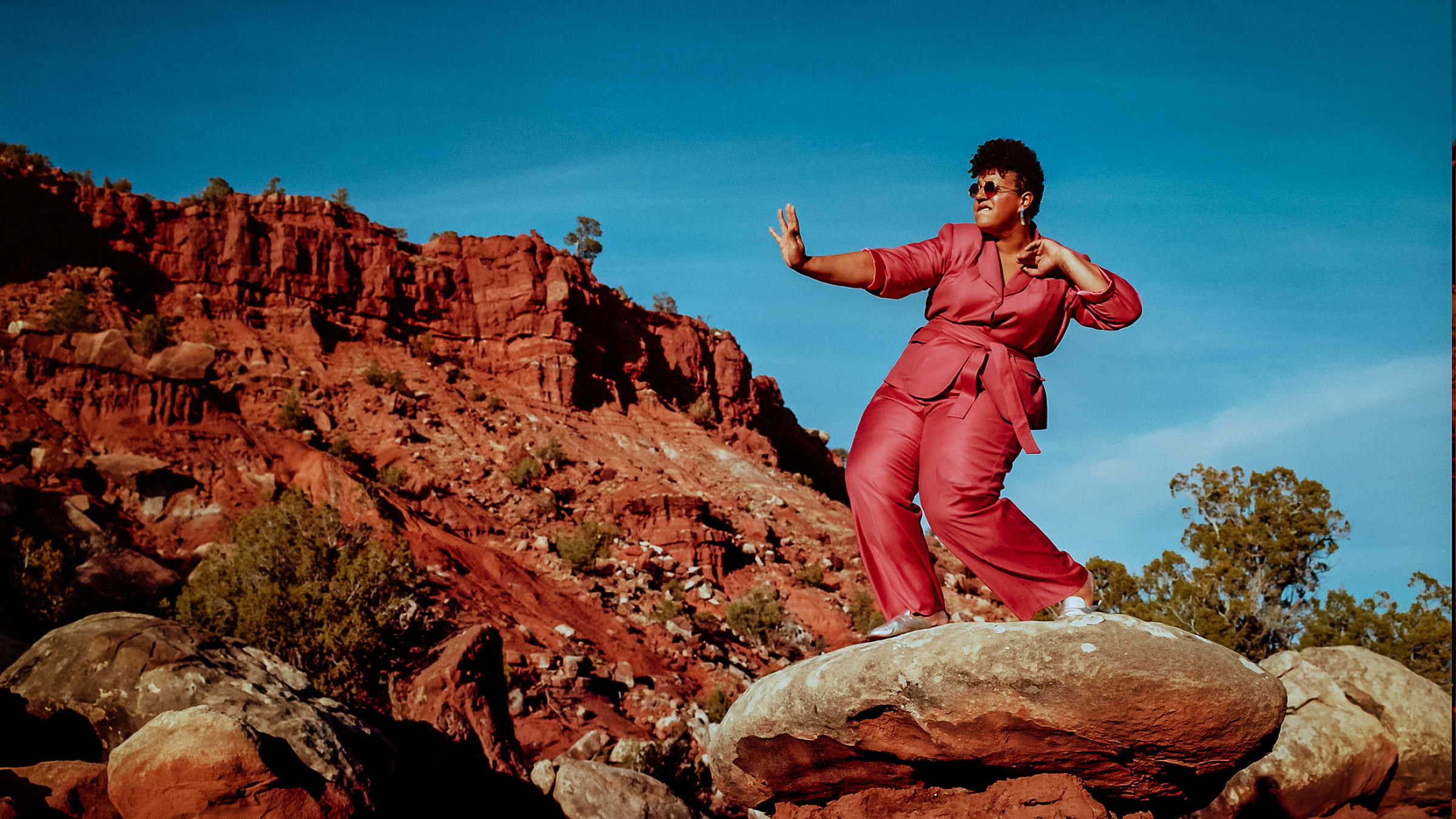 "Brittany Howard: In concert": Eine Frau mit rostfarbenem Hosenanzug steht auf einem Stein in einer rot-braunen Felsenlandschaft. Sie macht eine Bewegung wie ein Karatekämpfer.