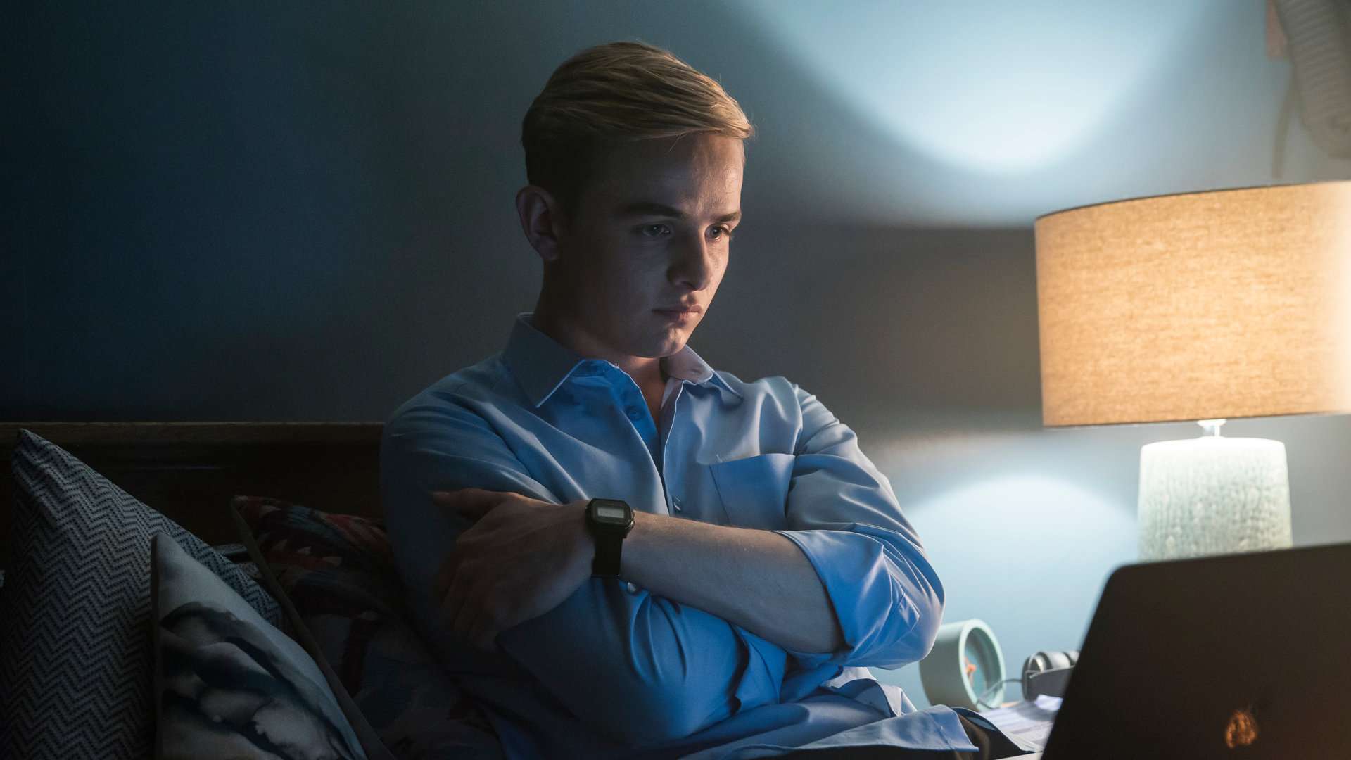"Alex Rider - Geheimnis": Alex Rider (Otto Farrant) sitzt in seinem Bett und hält verschränkt die Arme vor seiner Brust. Mit ernstem Gesichtsausdruck blickt er auf den Bildschirm eines Laptops vor sich.