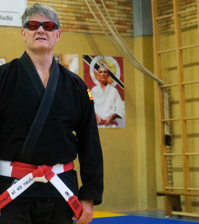 "einfach Mensch - Juan de la Fuente Briones: Mach dich stark":  Juan de la Fuente Briones steht in schwarzer Sportbekleidung mit einer dunklen Brille in einer Sporthalle.