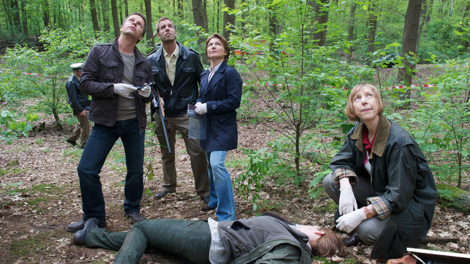 "SOKO Wismar - Hochwild": In einem Waldstück liegt eine Leiche. Dr. Helene Sturbeck (Katharina Blaschke) sitzt an deren Kopf. Ein Stück weiter hinten stehen Sven Herzog (Michael Härle), Lars Pöhlmann (Dominic Boeer) und Katrin Börensen (Claudia Schmutzler). Alle schauen nach oben.