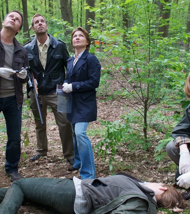 "SOKO Wismar - Hochwild": In einem Waldstück liegt eine Leiche. Dr. Helene Sturbeck (Katharina Blaschke) sitzt an deren Kopf. Ein Stück weiter hinten stehen Sven Herzog (Michael Härle), Lars Pöhlmann (Dominic Boeer) und Katrin Börensen (Claudia Schmutzler). Alle schauen nach oben.