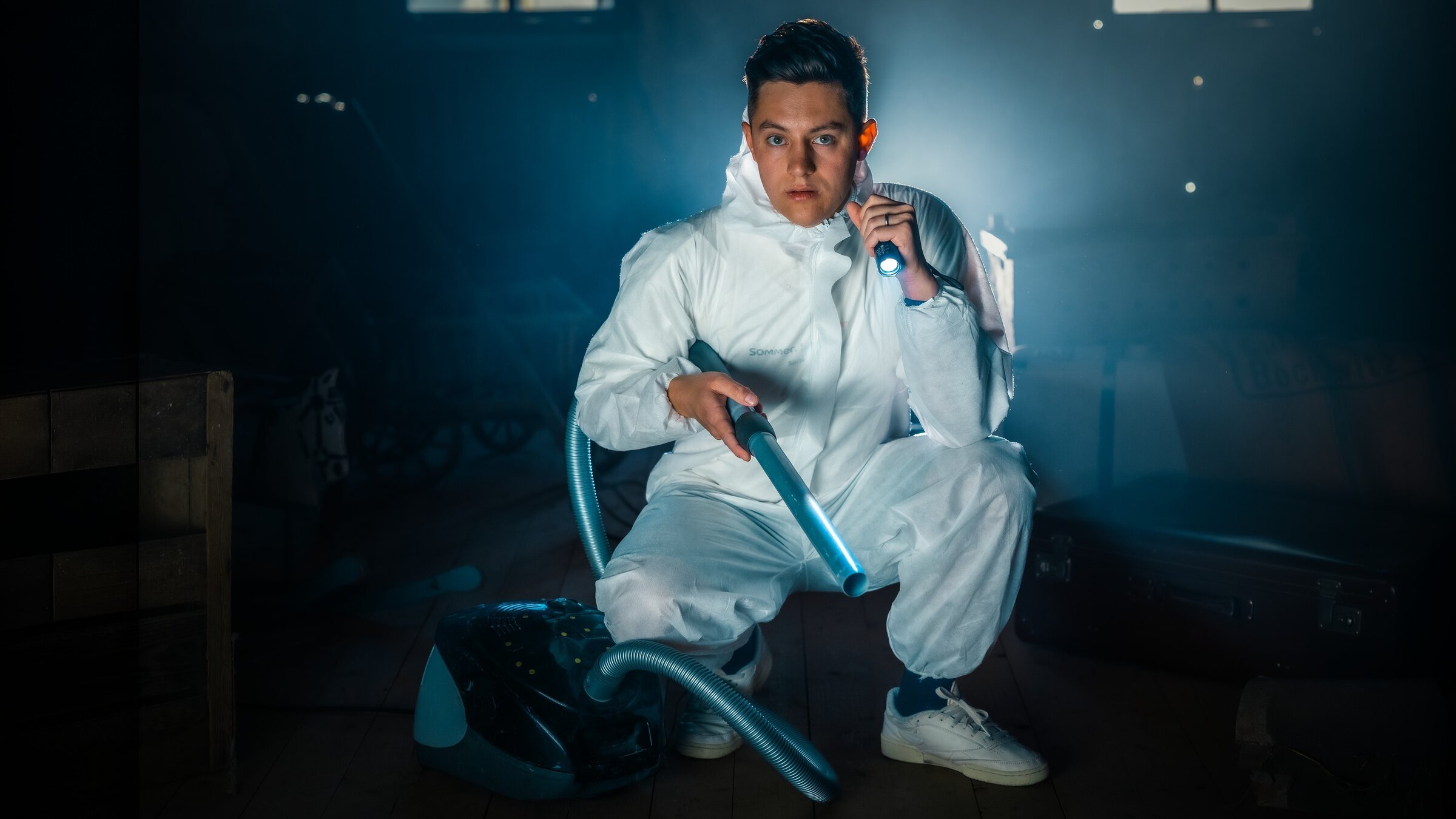 "37Â°Leben - Against all Gods: Die HÃ¶lle Ã¶ffnet sichâ: Denis, gekleidet in einem Schutzanzug gekleidet, hockt in einem dunklen Raum auf dem Boden. In der einen Hand hÃ¤lt er eine Taschenlampe, in der anderen den Schlauch eines Staubsaugers.