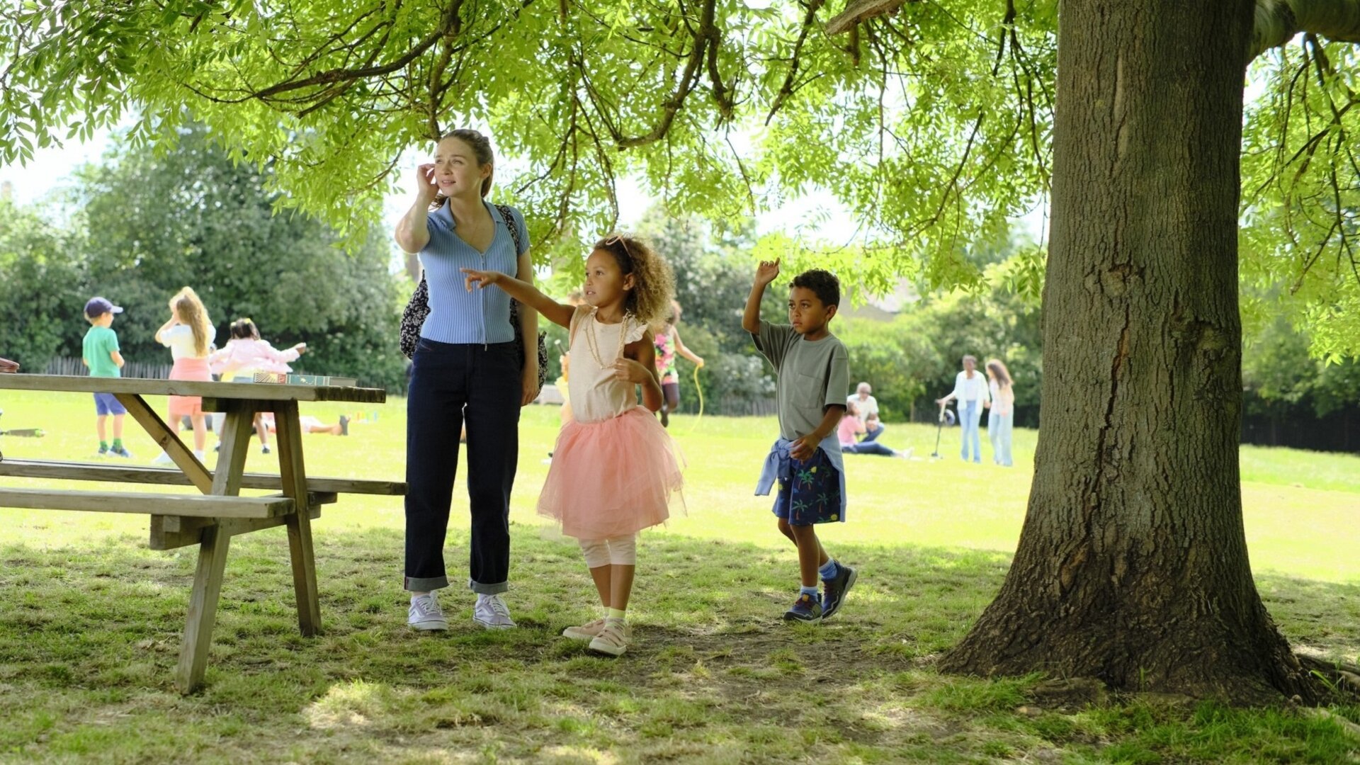 "You & Me": Emma (Jessica Barden) steht im Park und schaut sich verwirrt um, während die Kinder Poppy (Isabella Tyson) und Jack (Lucas Tyson) neben ihr stehen und entschlossen in eine Richtung zeigen.