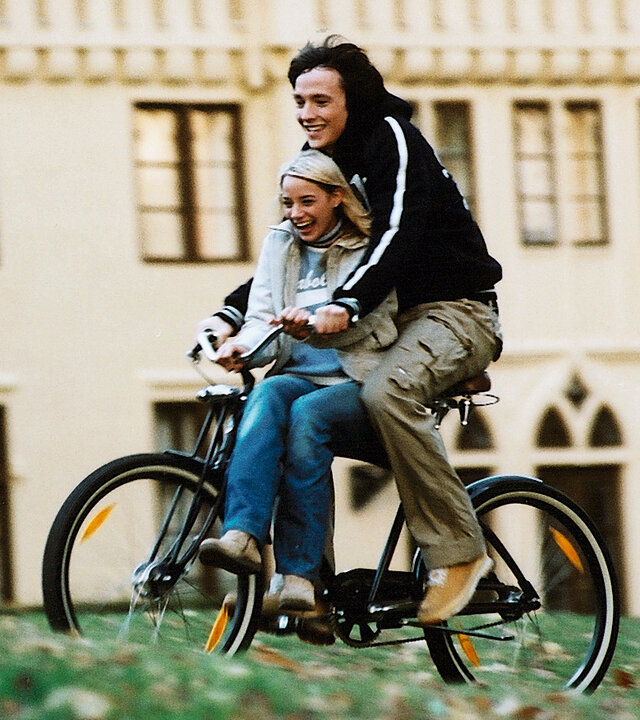 "Bianca - Wege zum Glück: Folge 65": Vor dem Gutshof: Sofia (Jytte-Merle Böhrnsen) sitzt vorne auf dem Fahrrad. Heiko (Ralph Kretschmar) fährt das Fahrrad. Sie lachen beide und scheinen Spaß zu haben.