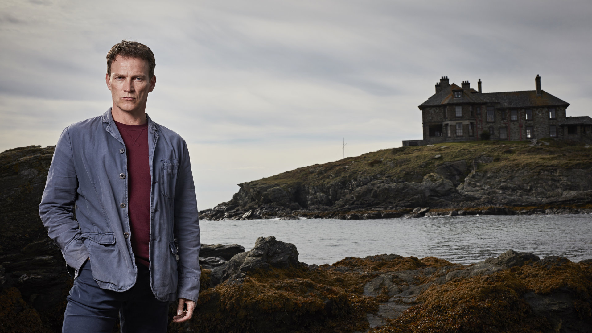 "Safe House - Entführung": Tom Brook (Stephen Moyer) steht vor einer Küste und schaut ernst in die Kamera. Im Hintergrund ist ein großes Haus zu sehen.