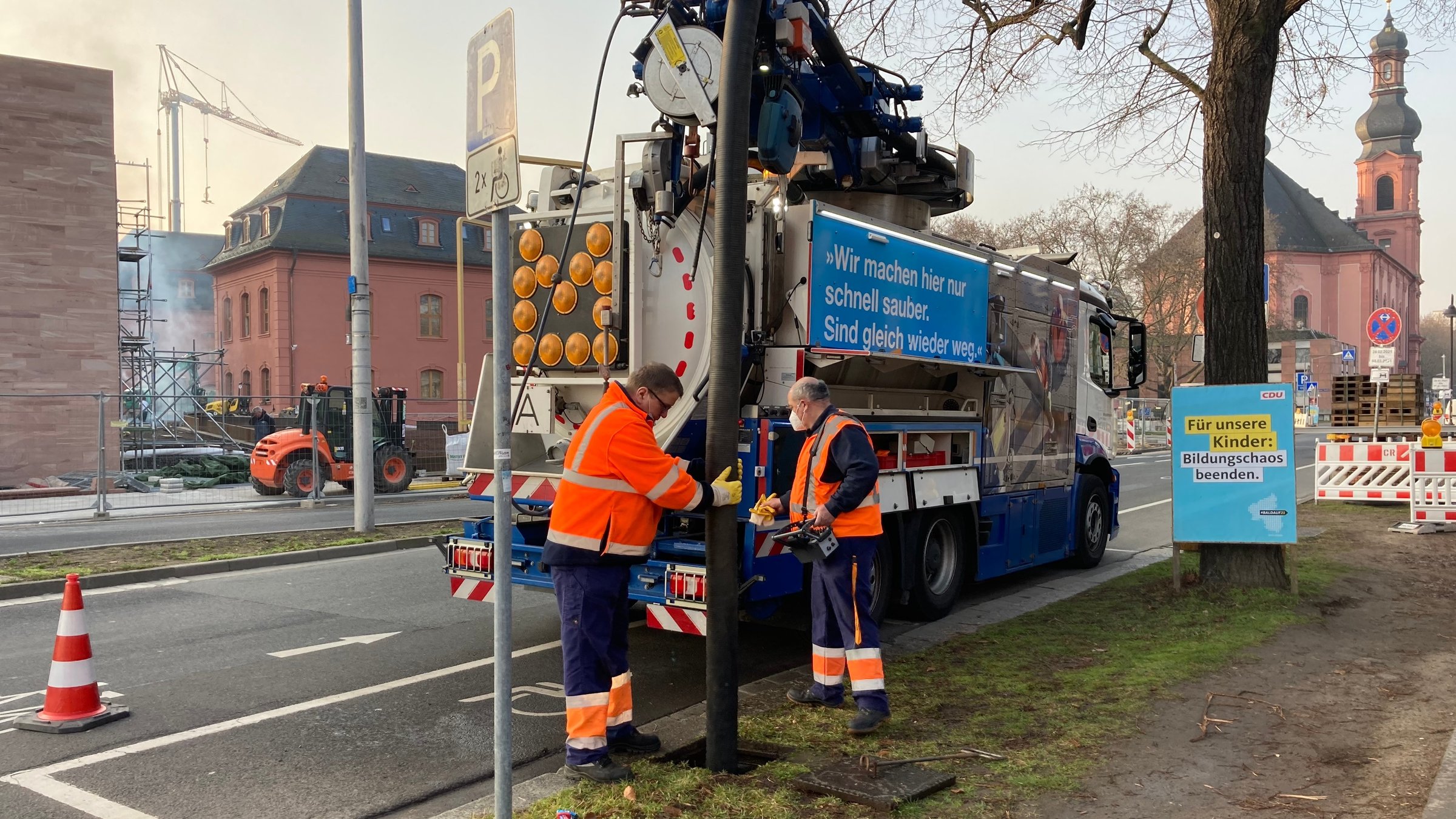 "ZDF.reportage: Kanalhelden - Arbeiten im Abwasser": Zwei Kanalreiniger stehen mit ihren Reinigungsfahrzeug am Straßenrand. Mit einem Spezialschlauch saugen sie Dreck aus einem Gulli.