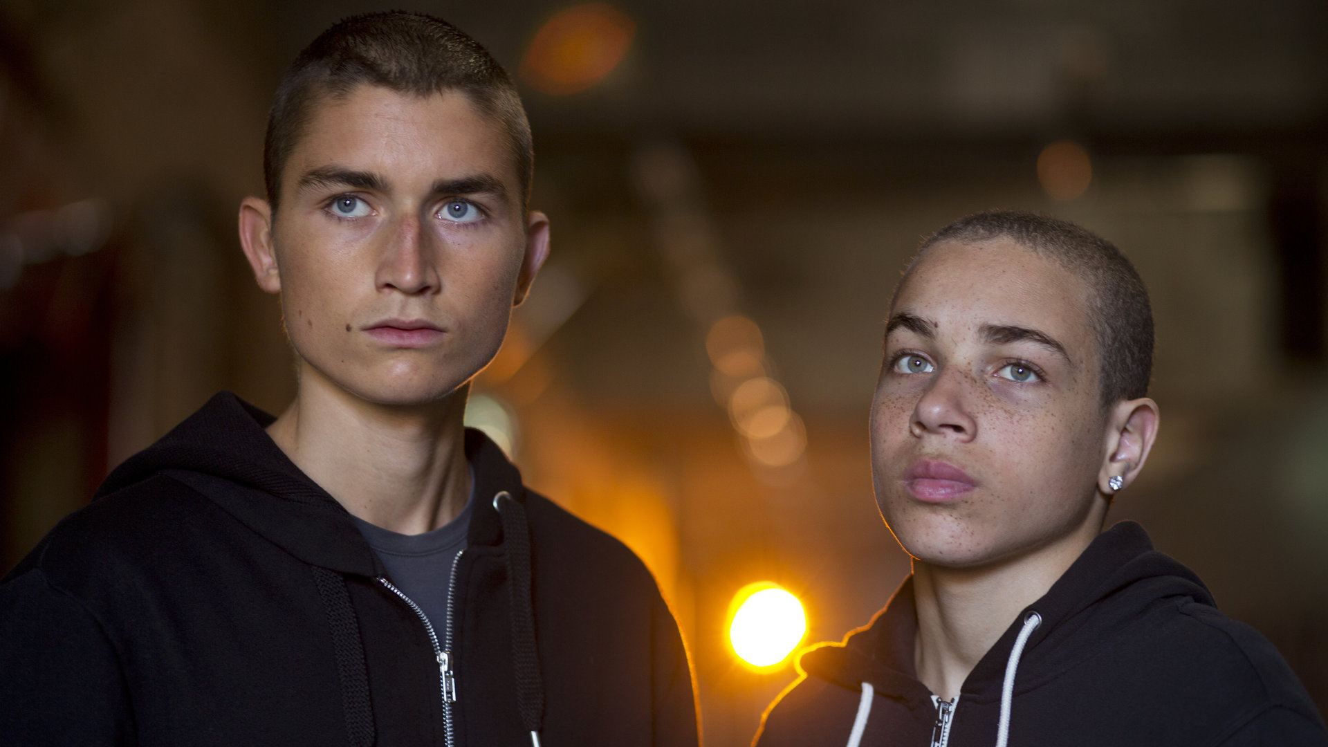 "Springflut - Vergeltung": Liam (Gustav Lindh) und Adam (Dakota Trancher Williams) stehen in dunklen Sweatshirt-Jacken mit Kapuzen in einem Keller, und ihr ernster Blick schweift in die Ferne.