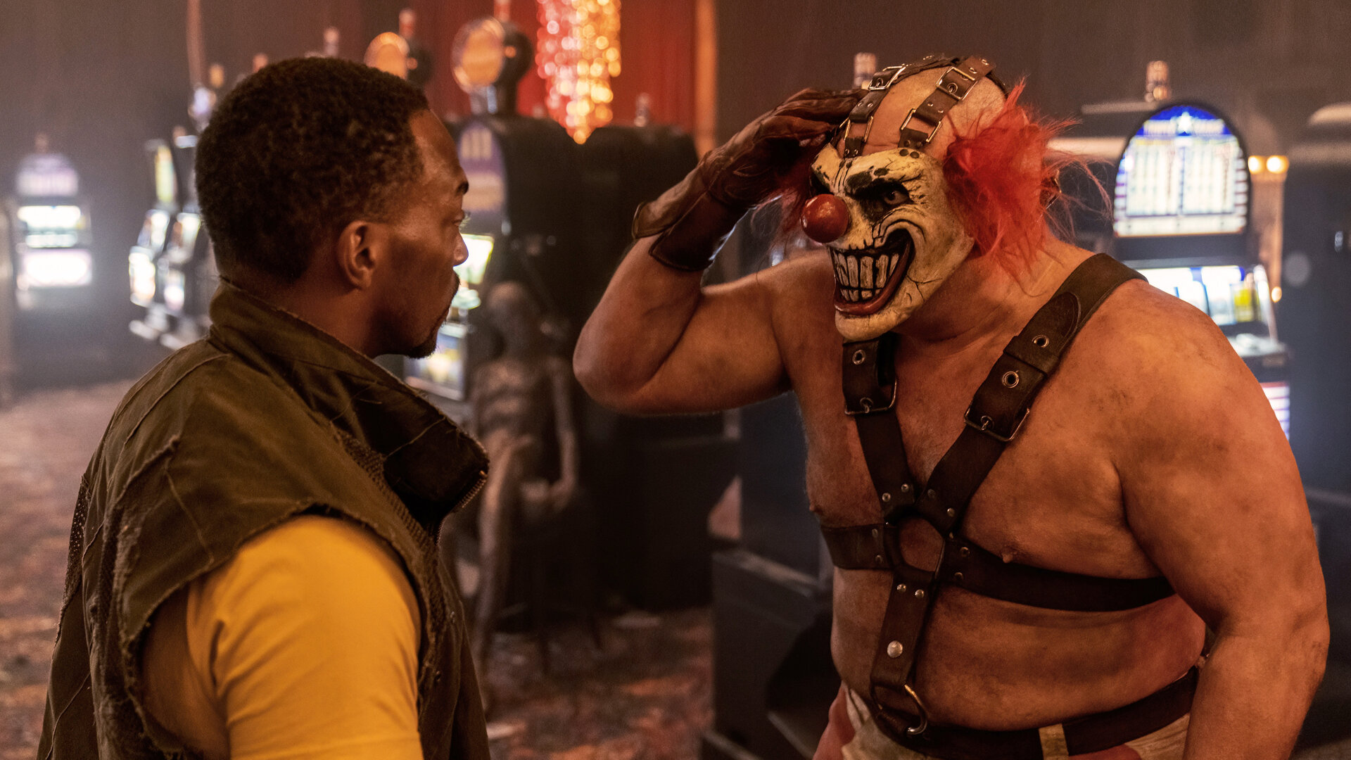 "Twisted Metal - 3RNCRCS": John (Anthony Mackie) steht Sweet Tooth (Joe Seanoa) gegenüber, der sich mit einem braunen Lederhandschuh an den Kopf fasst. Im Hintergrund sind Spielautomaten zu erkennen.