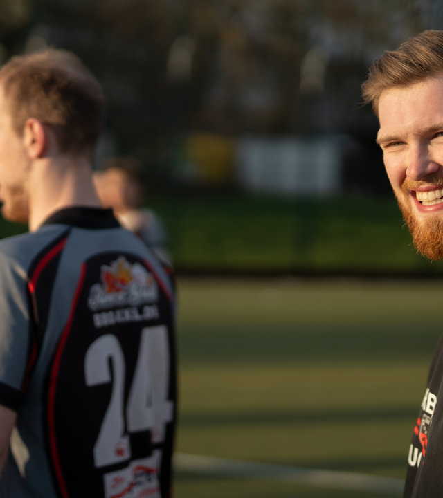 „einfach Mensch - Henry Mackney: Im Team unschlagbar": Henry Mackney wird von der untergehenden Sonne angestrahlt und lacht, weiterer Teamkollege steht im Trikot daneben.