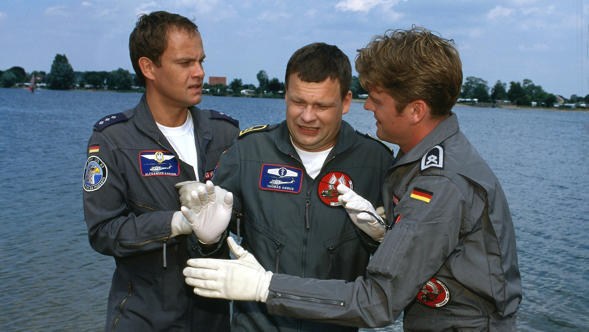 "Die Rettungsflieger - Abschied von Thomas": Alex (Matthias Leja) und Wollcke (Oliver Hörner) stehen rechts und links von dem verzweifelt schauenden Thomas (Ulrich Bähnk). Hinter ihnen der See.