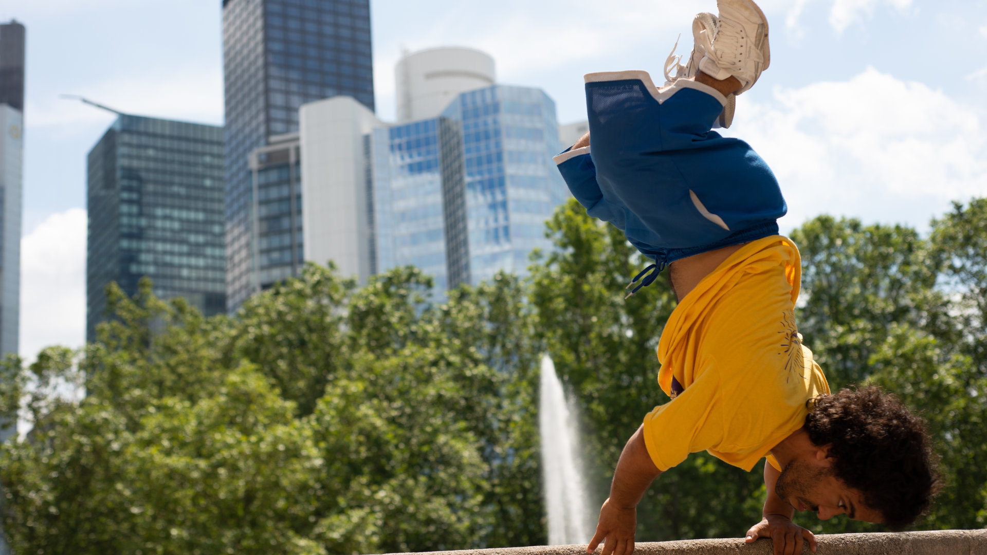 "Einfach Mensch - Mach Dein Ding": Ihab Yassin macht einen Handstand auf einer Mauer. Im Hintergrund eine Skyline.