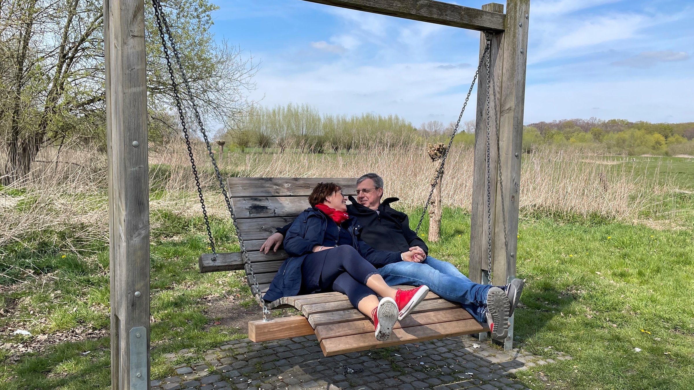 "37° Wir retten unsere Ehe": Tanja und Dirk Sorgalla sitzen nebeneinander auf einer großen, geschwungenen Holzschaukel. Im Hintergrund sieht man weitläufige Wiesen und Sträucher. Er hat den Arm um sie gelegt, sie schmiegt sich an ihn, die beiden lächeln sich an.