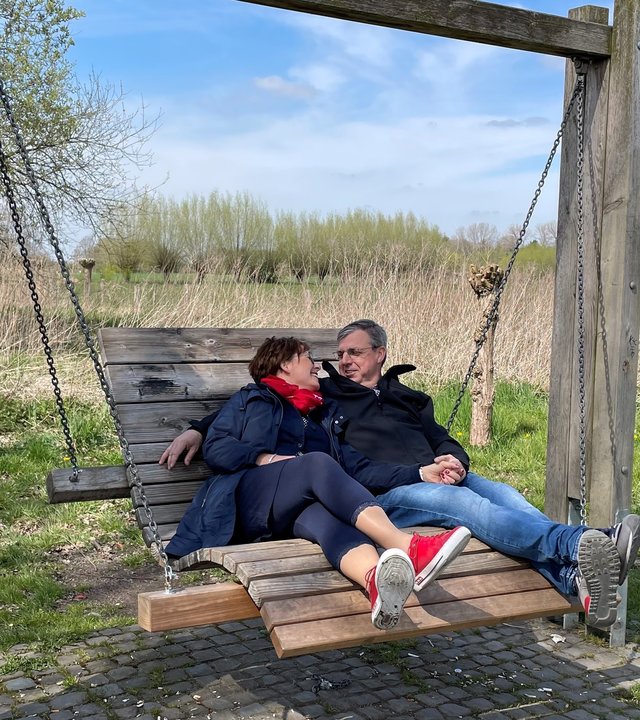 "37° Wir retten unsere Ehe": Tanja und Dirk Sorgalla sitzen nebeneinander auf einer großen, geschwungenen Holzschaukel. Im Hintergrund sieht man weitläufige Wiesen und Sträucher. Er hat den Arm um sie gelegt, sie schmiegt sich an ihn, die beiden lächeln sich an.