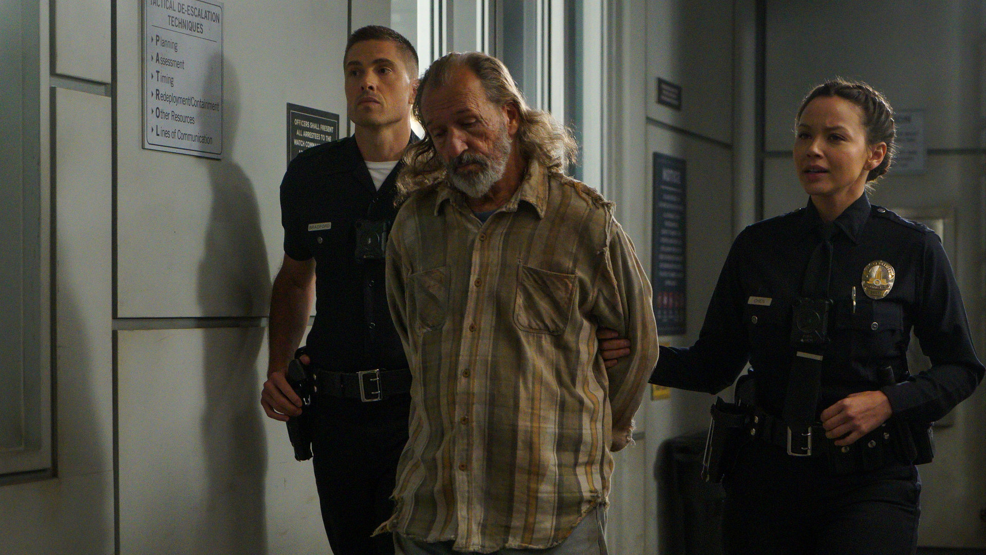 "The Rookie - Hollywood auf Streife": Tim Bradford (Eric Winter) und Lucy Chen (Melissa O'Neil) laufen einen Gang im Gefängnis entlang. In ihrer Mitte halten sie einen Straftäter fest.