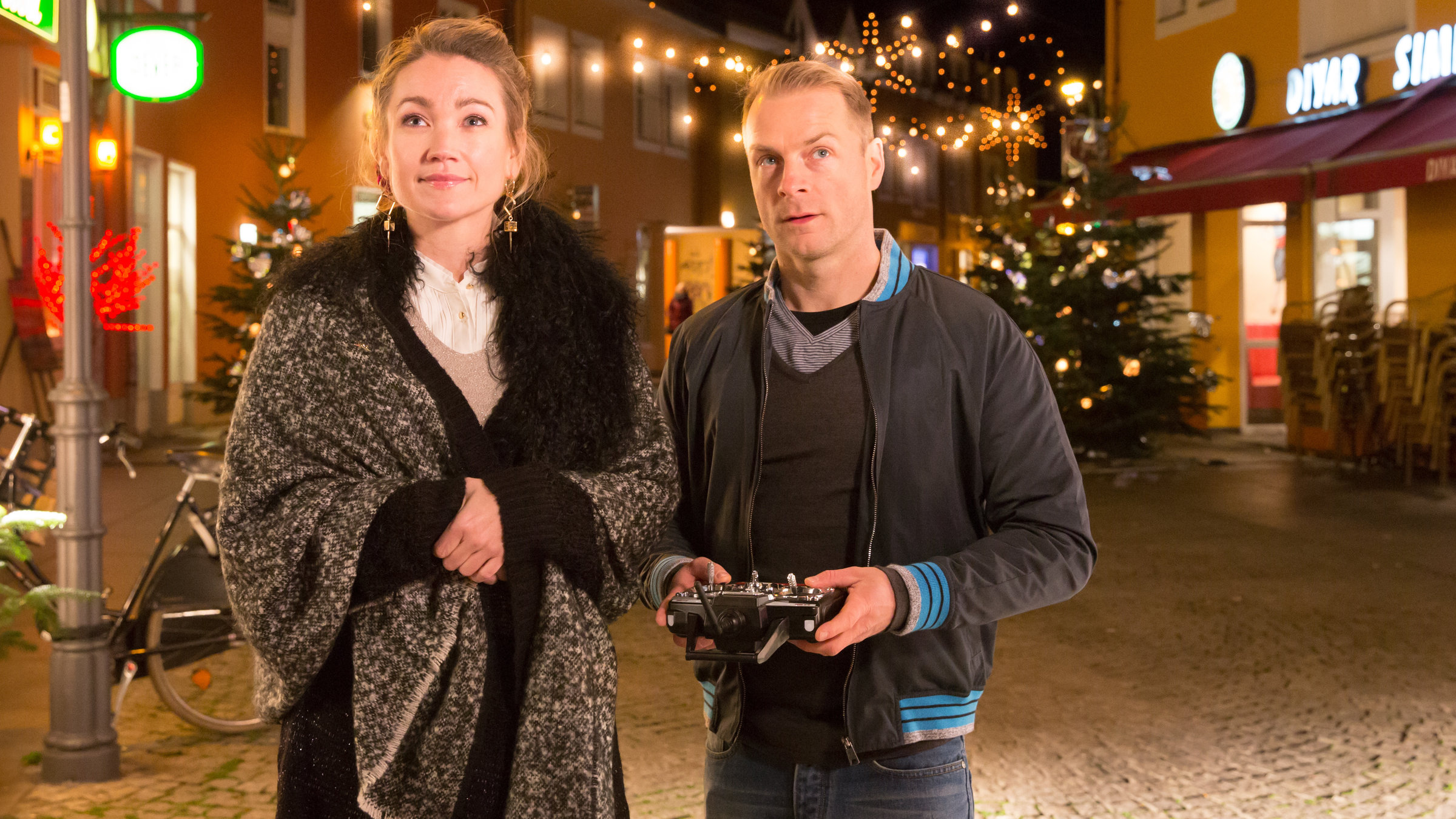 "Der mit dem Schlag": Melanie Merk (Lisa Maria Potthoff) und Felix Grünler (Hinnerk Schönemann) stehen nebeneinander auf einer weihnachtlich beleuchteten Straße. Felix hat eine Fernbedienung in seinen Händen. Er und Melanie schauen erwartungsvoll nach vorne.