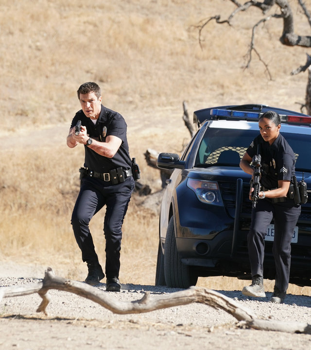 "The Rookie - Tag des Todes": Schwer bewaffnet stürmen John Nolan (Nathan Fillion) und Nyla Harper (Mekia Cox) aus dem Polizeiauto auf das Grundstück in der Wüste.