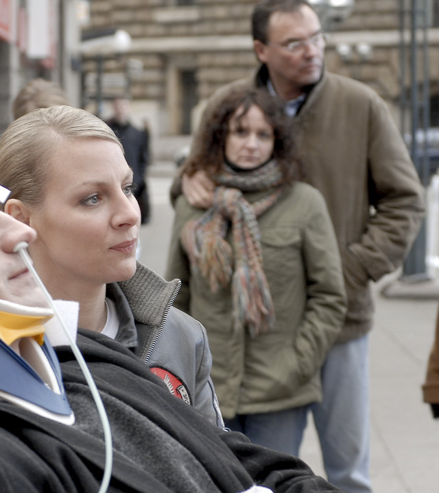 "Die Rettungsflieger - Neuanfänge": Christian Baumann (Simon Böer) liegt auf einer Krankentrage. Bettina (Suzanne Kockat) steht daneben und sieht ihn besorgt an. Sabine (Marlene Marlow) steht daneben und beobachtet die beiden.