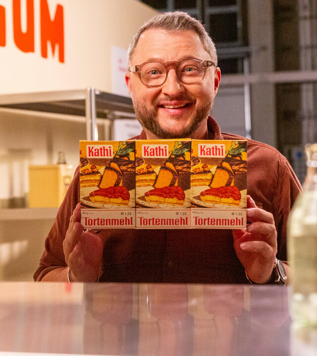 "besseresser: Die Tricks in DDR-Produkten - Sebastian Lege deckt auf": Sebastian Lege hält drei Packungen des Kathi-Tortenmehls in die Kamera.