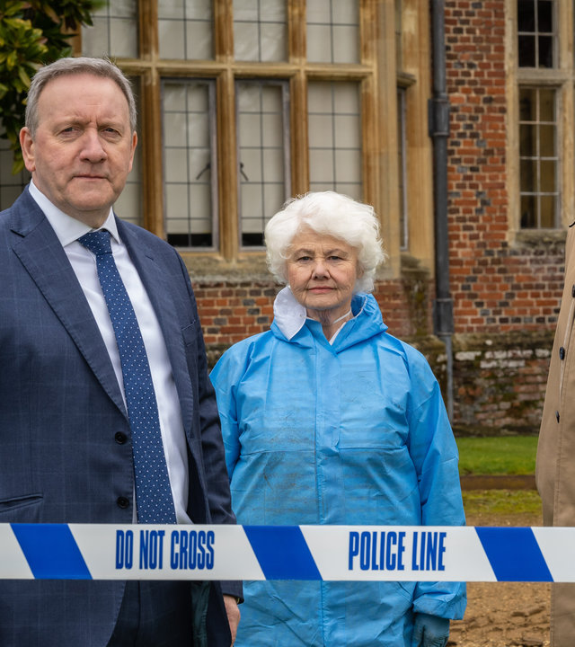 "Inspector Barnaby - Der Untergang des Hauses Shirewell": DCI John Barnaby (Neil Dudgeon), gekleidet in einem dunkelblauen Anzug mit weißem Hemd und blauweißgepunkteter Krawatte, Rechtsmedizinerin Fleur Perkins (Annette Badland), gekleidet in einem blauen Plastikoverall, und DS Jamie Winter (Nick Hendrix), gekleidet in einem beigefarbenen Mantel und grauer Hose, stehen hinter einem blauweißen Polizeiabsperrband.