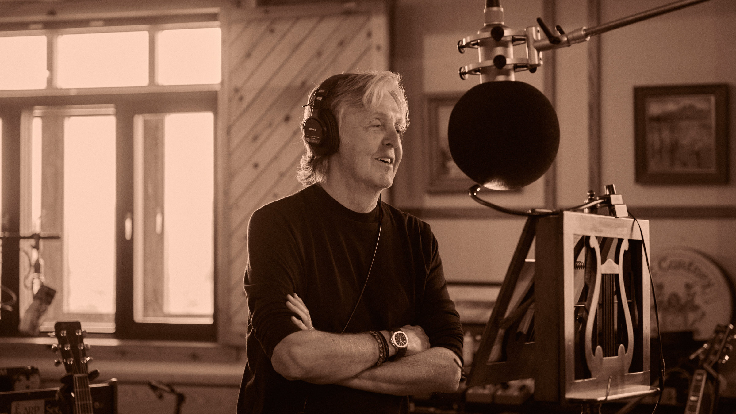 "Paul McCartney & Wings: Rockshow": Paul McCartney steht mit verschränkten Armen vor einem Aufnahmemikrofon. Er trägt Kopfhörer. Vor ihm steht ein antikes Notenpult aus Holz (s/w).