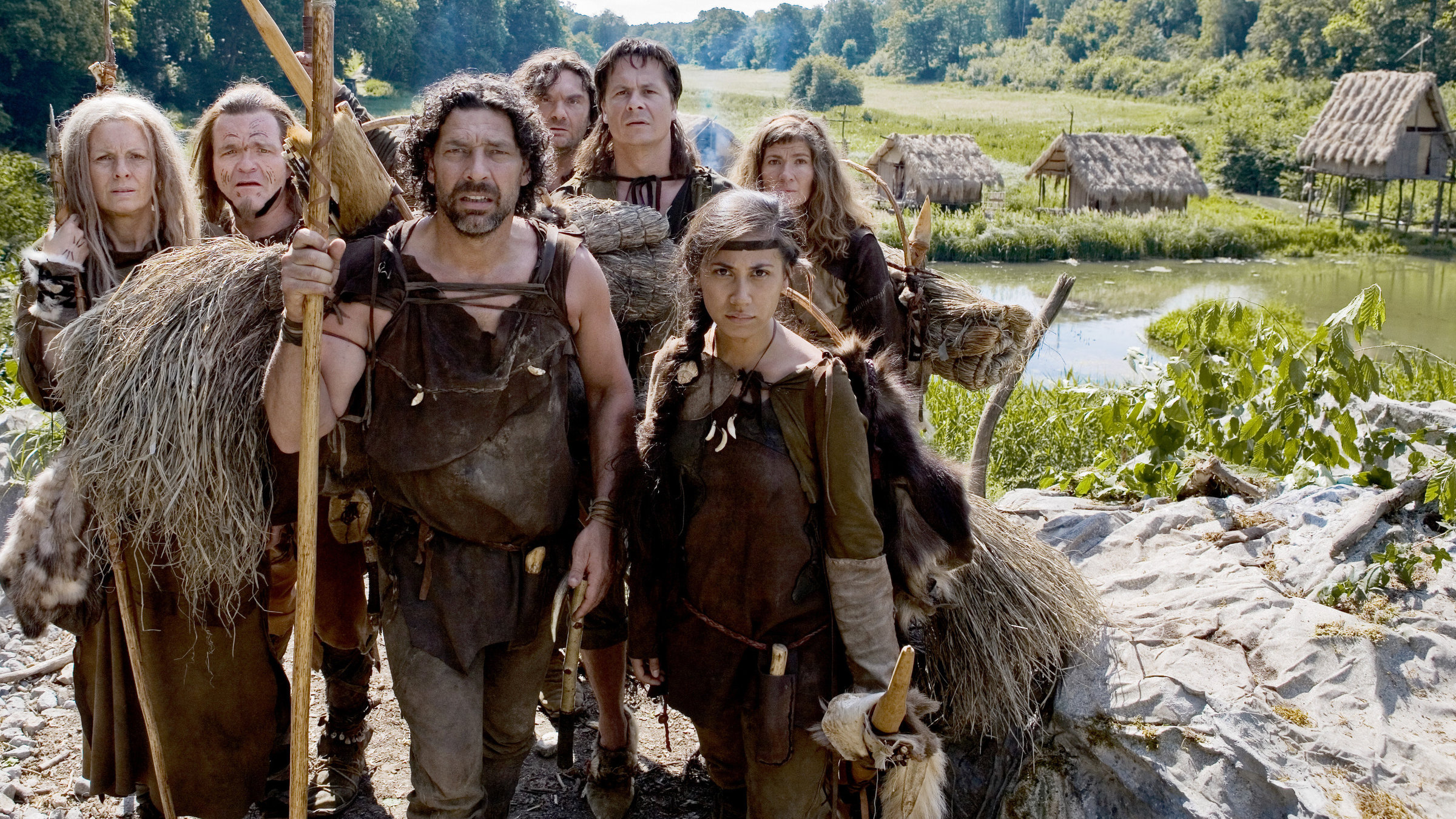 "Die Steintaler - von wegen Homo sapiens (1/12)": Gruppenbild (v.li.): Ulli Maier (Avlis), Cornelius Obonya (Guruk), Gregor Bloéb (Meso), Martin Leutgeb (Gulo), Michael Dangl (Retila), Maya Henselek (Alva), Carmen Gratl (Bele). Im Hintergrund stehen ein paar Hütten.