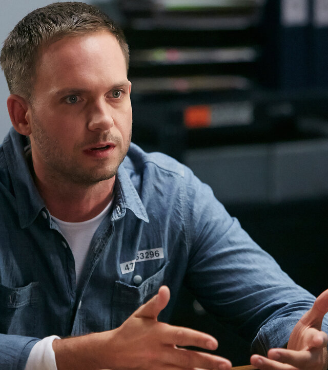 "Suits - Vertrauen": Mike (Patrick J. Adams) sitzt an einem Tisch während er spricht und gestikuliert. Er schaut ernst nach vorne.
