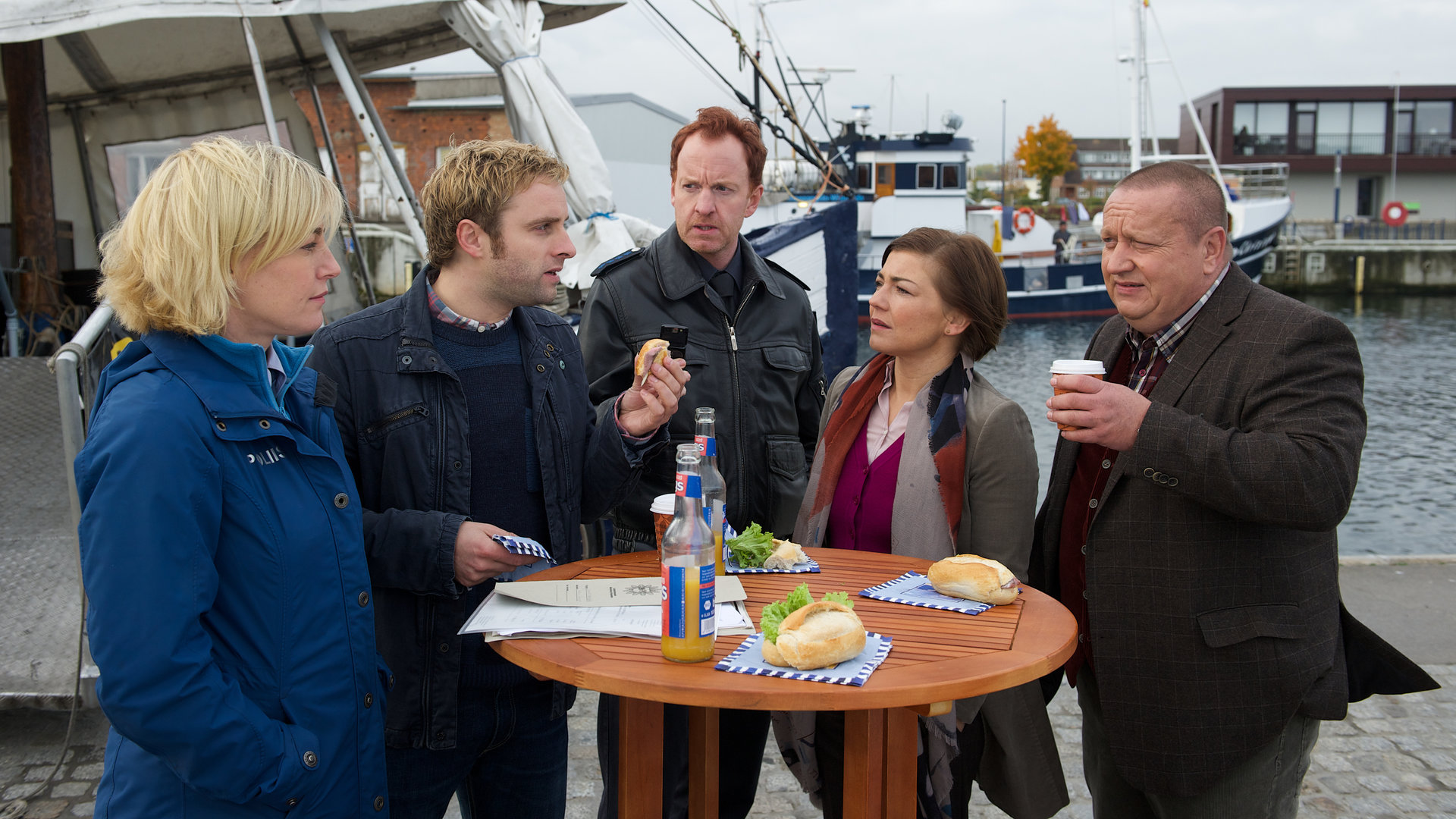 "SOKO Wismar - Das Nashorn": Leena Virtanen (Li Hagman), Nils Theede (Jonas Laux),  Kai Timmermann (Mathias Junge), Katrin Börensen (Claudia Schmutzler) und Jan Reuter (Udo Kroschwald) stehen nebeneinander an einem Stehtisch am Hafen. Vor ihnen stehen Getränkeflaschen und Brötchen.