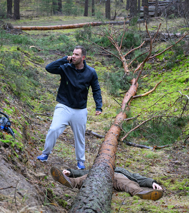 "SOKO Wismar - Holz fällt!": Lars Pöhlmann (Dominic Boeer) steht im Wald neben der Leiche von Alexander Hübner (Odysseas J. Hlepas) und telefoniert.
