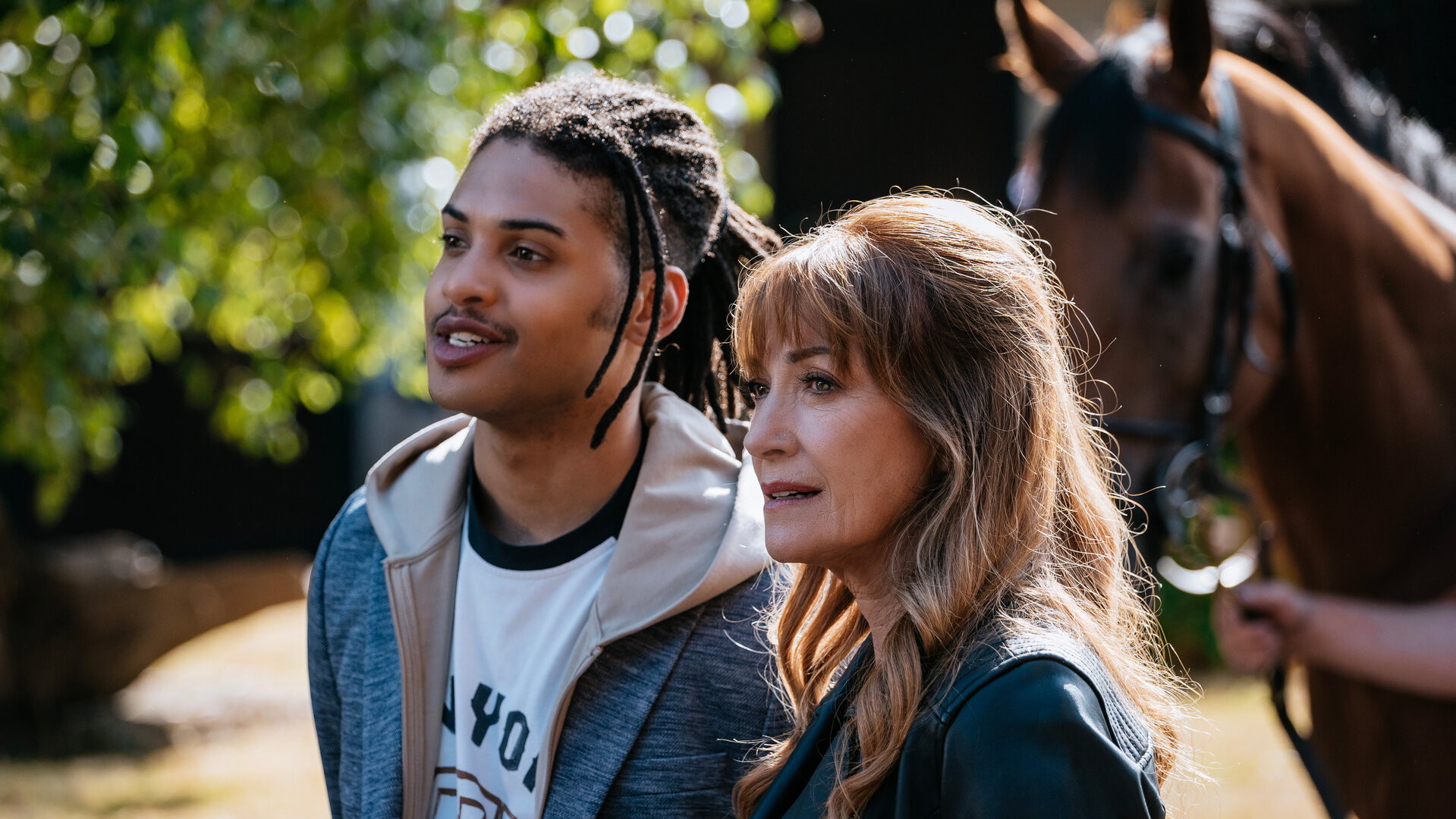 "Harry Wild – Mörderjagd in Dublin - Die Geschichte vom toten Pferd": Fergus Reid (Rohan Nedd) und Harry Wild (Jane Seymour) stehen nebeneinander im Freien. Hinter ihnen ist in der Unschärfe ein Pferd zu erkennen.