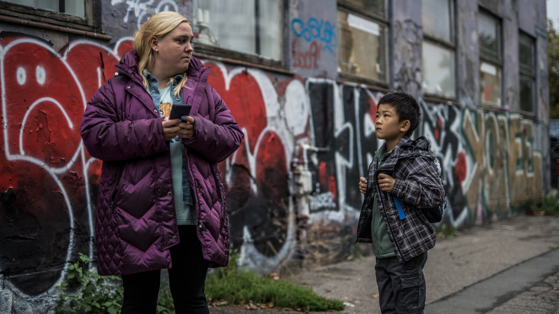 "Elvira - Sun": Elvira (Sara Klein) und der kleine Junge Sun (Oliver Ye Lu) stehen vor einer mit Graffiti beschmierten Hauswand.
