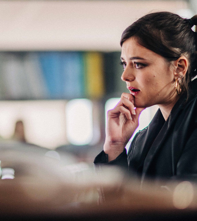 "Survivors - Ein Stück Wahrheit": Léa (Adèle Wismes) sitzt in einer Bibliothek vor einem Computer und sieht nachdenklich nach vorne.