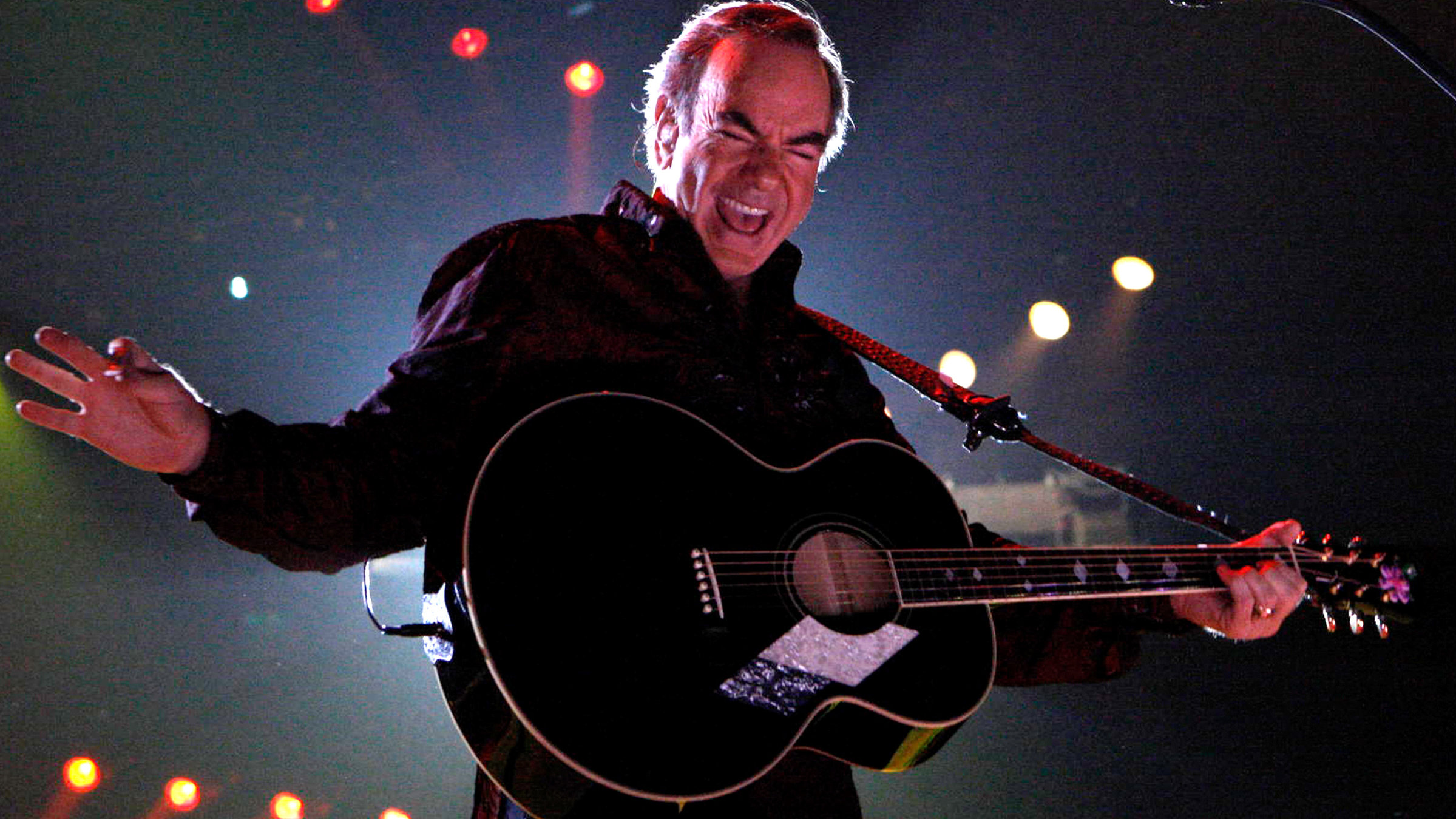 "Neil Diamond: Thank You Australia": Neil Diamond steht singend auf einer Bühne. Die Gitarre hat er um die Schulter gebunden. Die linke Hand hält den Gitarrenhals. Den rechten Arm ist zur Seite ausgestreckt.