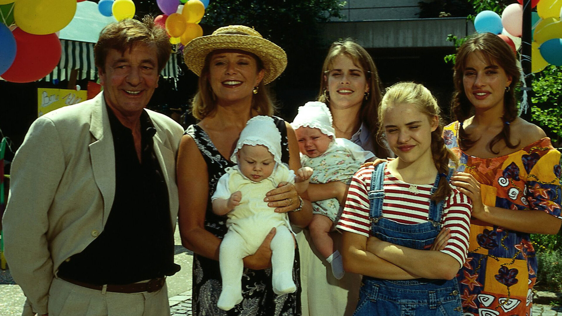 "Alle meine Töchter - Duplizität der Ereignisse": Dr. Berthold Sanwaldt (Günter Mack), Margot Sanwaldt (Jutta Speidel), Dr. Anna Sanwaldt (Ursula Buschhorn), Patricia Sanwaldt (Fritzi Eichhorn) und Sylvie von Wettenberg (Julia Dahmen) und die beiden Babys Jenin und Verena stehen auf einem Schulhof freudig lächelnd nebeneinander.