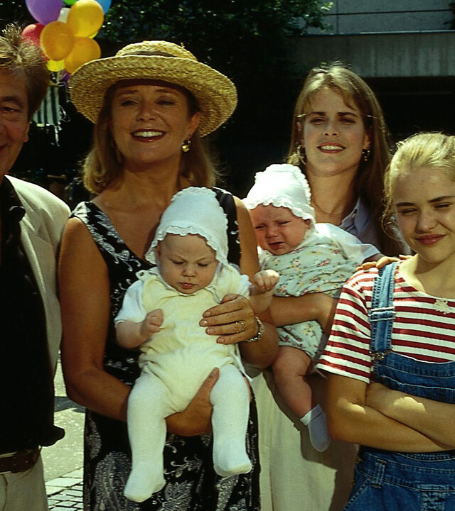 "Alle meine Töchter - Duplizität der Ereignisse": Dr. Berthold Sanwaldt (Günter Mack), Margot Sanwaldt (Jutta Speidel), Dr. Anna Sanwaldt (Ursula Buschhorn), Patricia Sanwaldt (Fritzi Eichhorn) und Sylvie von Wettenberg (Julia Dahmen) und die beiden Babys Jenin und Verena stehen auf einem Schulhof freudig lächelnd nebeneinander.