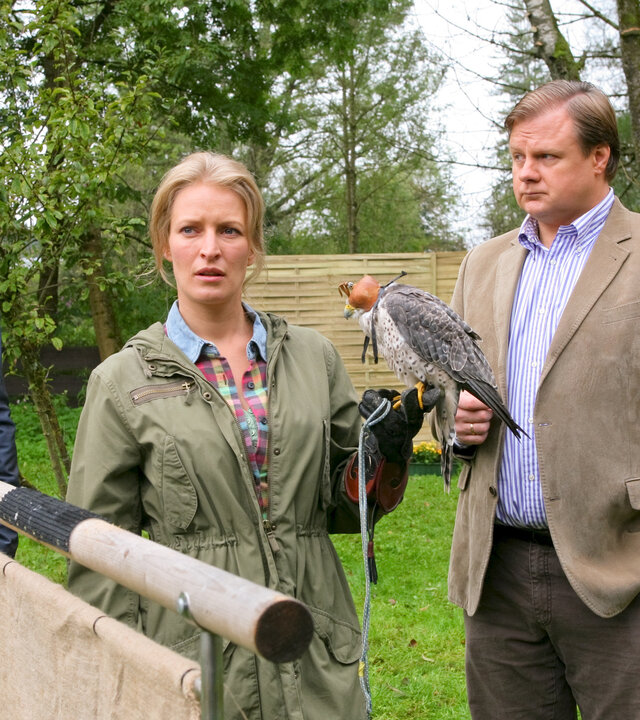 "Die Rosenheim-Cops - Ausgeflogen": Die Kommissare Hartl (Michael A. Grimm), Hansen (Igor Jeftic) und Polizist Mohr (Max Müller) befragen Sandra Holzinger (Stefanie von Poser), die einen Greifvogel auf der Hand hält.