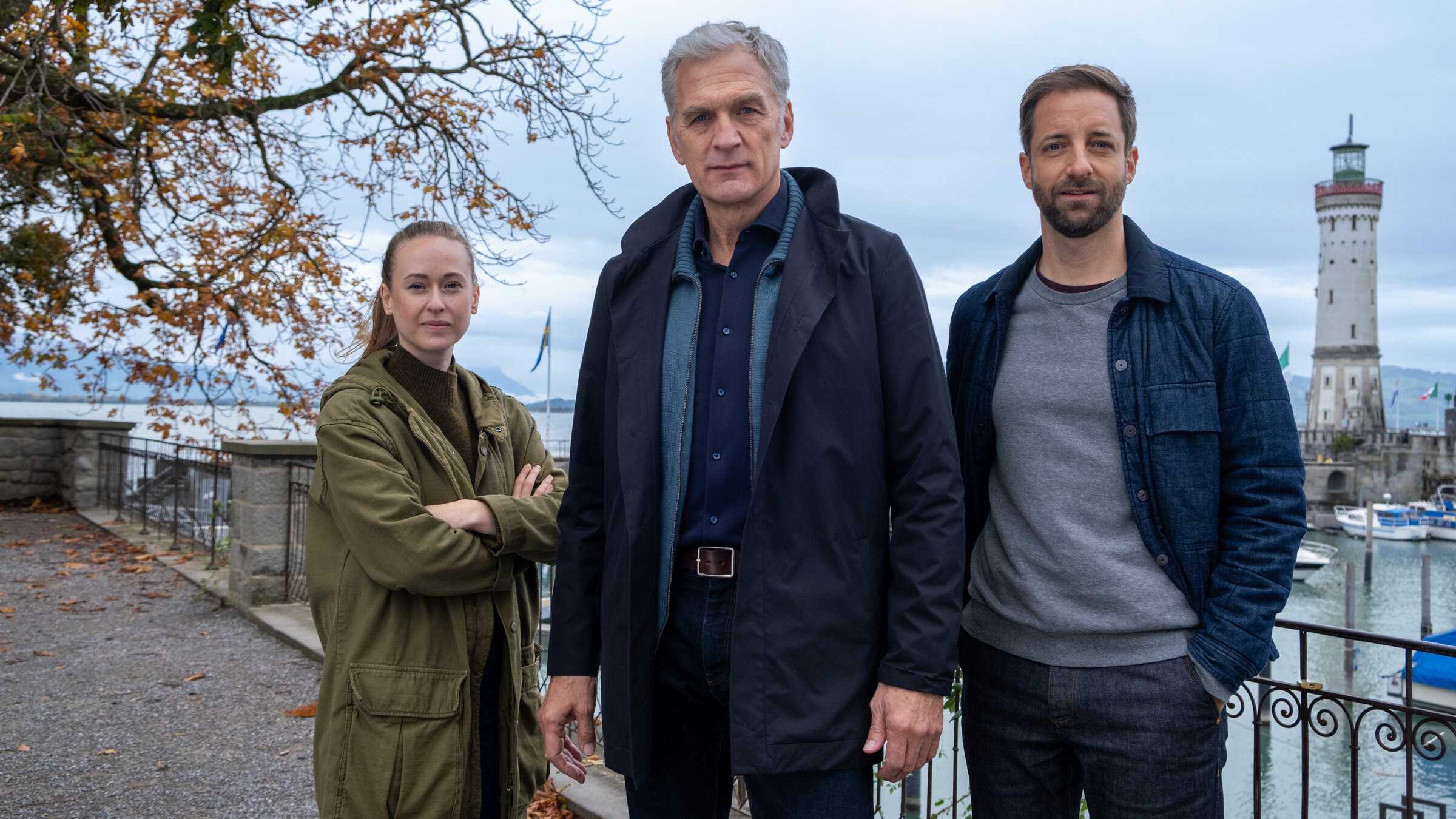 "Der Kommissar und der See - In besseren Kreisen": Annika Wagner (Nurit Hirschfeld), Robert Anders (Walter Sittler) und Martin Keller (Dominik Maringer) stehen nebeneinander am Ufer des Sees und schauen in die Kamera.