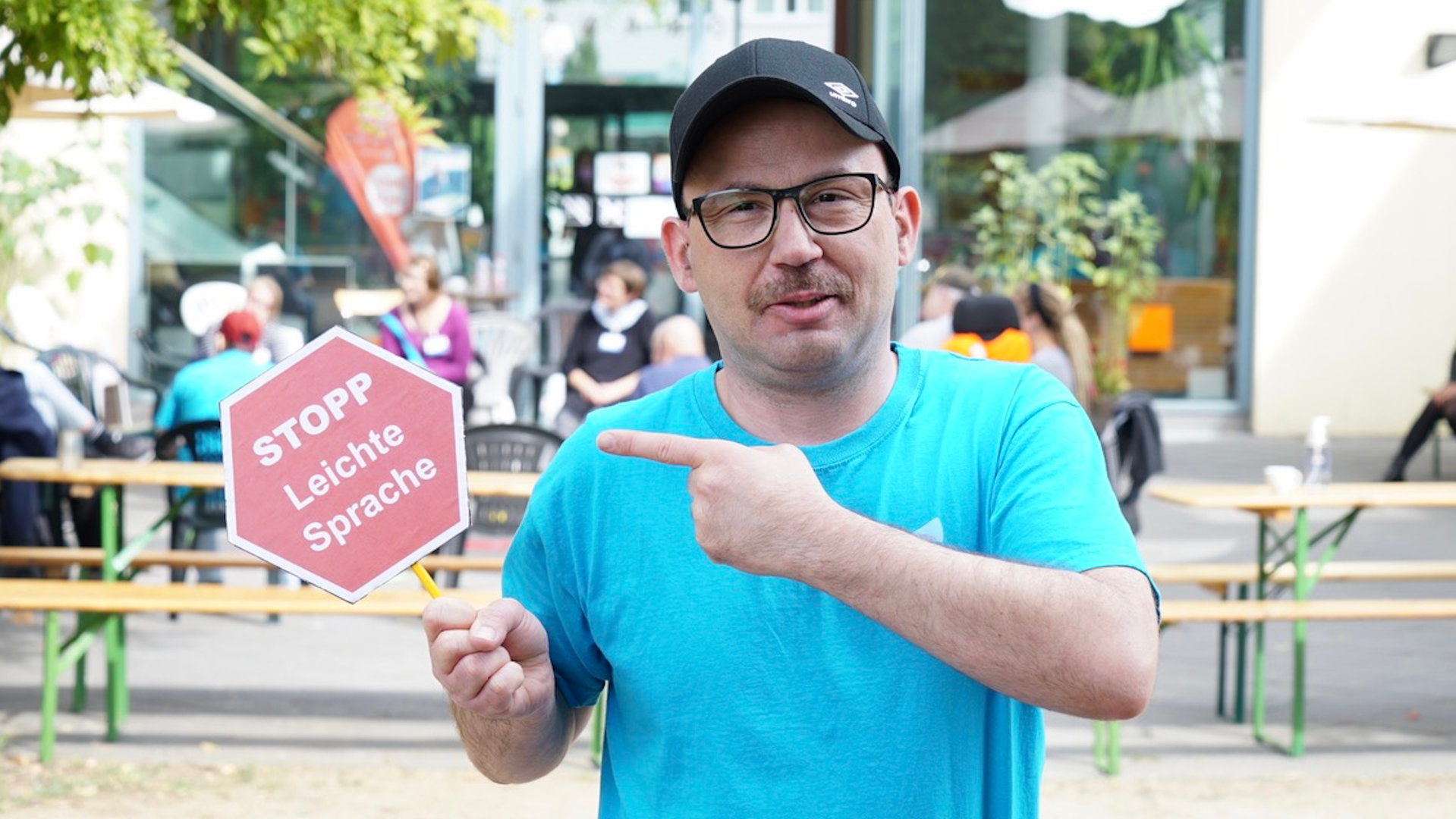 "einfach Mensch: Wir haben die Wahl - Es geht um uns": Sascha Ubrig hält ein Schild hoch auf dem "Stopp: Leichte Sprache" steht. Eine Forderung von Menschen mit Behinderung, Texte so verständlich wie möglich zu gestalten.