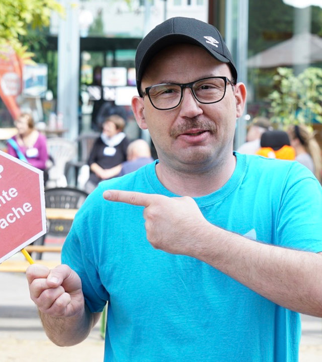 "einfach Mensch: Wir haben die Wahl - Es geht um uns": Sascha Ubrig hält ein Schild hoch auf dem "Stopp: Leichte Sprache" steht. Eine Forderung von Menschen mit Behinderung, Texte so verständlich wie möglich zu gestalten.