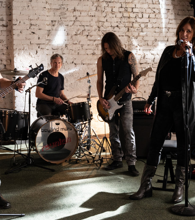 "SOKO Stuttgart - Reunion": Die Band "Beyond Mars" ist in ihrem Proberaum und macht Musik. Die Sängerin Lina Wagner (Carin C. Tietze) steht vorne am Mikrofon, der Bassist Gerry Brügge (Hansa Czypionka) etwas entfernt neben ihr und ebenso an einem Mikrofon. Hinter ihnen sieht man den Gitarristen Carlo Hahn (Alexander Scholpp) und den Schlagzeuger Florian "Flocke" Wagner (Felix Theissen). Um sie herum stehen unter anderem ein Keyboard, eine weitere Gitarre und mehrere Verstärker. Durch ein großes Fenster seitlich der Probebühne fällt Sonnenlicht ein.