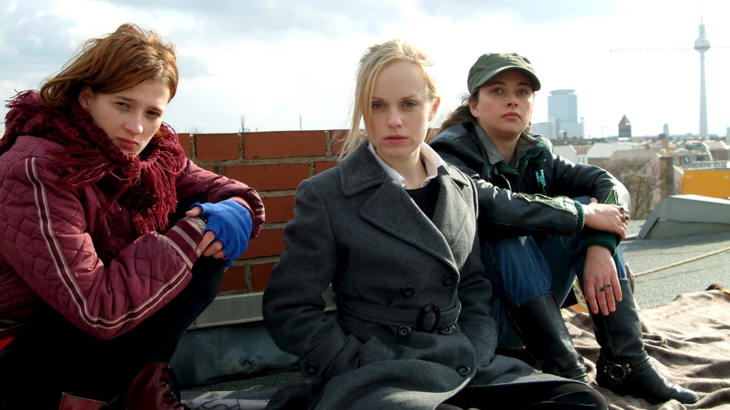 "Die Ex bin ich": Anne (Maria Kwiatkowsky), Sandra (Friederike Kempter) und Brit (Heike Warmuth) sitzen auf einem Dach und sehen angeschlagen aus. Im Hintergrund ist die Skyline von Berlin zu sehen.