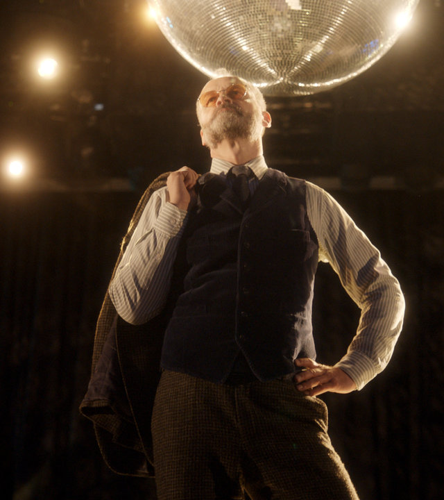"Agatha Christies Hjerson (1)": Mordermittler Sven Hjerson (Johan Rheborg) in eleganter Pose im glitzernden Licht eines Dancefloors.