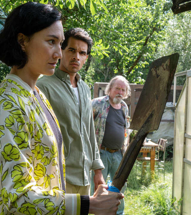 "SOKO Potsdam - Unkraut": Pauline Hobrecht (Agnes Decker) und Samir Amari (Skandar Amini) stehen zusammen mit Wolfgang Gerster (Paul Faßnacht) in dessen Garten. Samir und Wolfgang Gerster blicken zu Pauline, die sich eine Gartenschaufel anschaut.