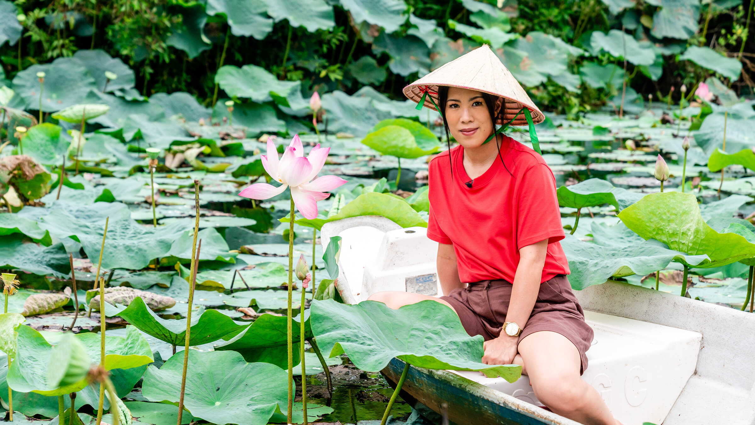 "Terra X: Vietnam - Eine Reise mit Mai Thi Nguyen-Kim": Mai sitzt auf einem kleinen Boot. Um sie herum sind überall grüne Wasserpflanzen. Neben Mai ragt eine große rosa Wasserlilie aus dem Wasser.