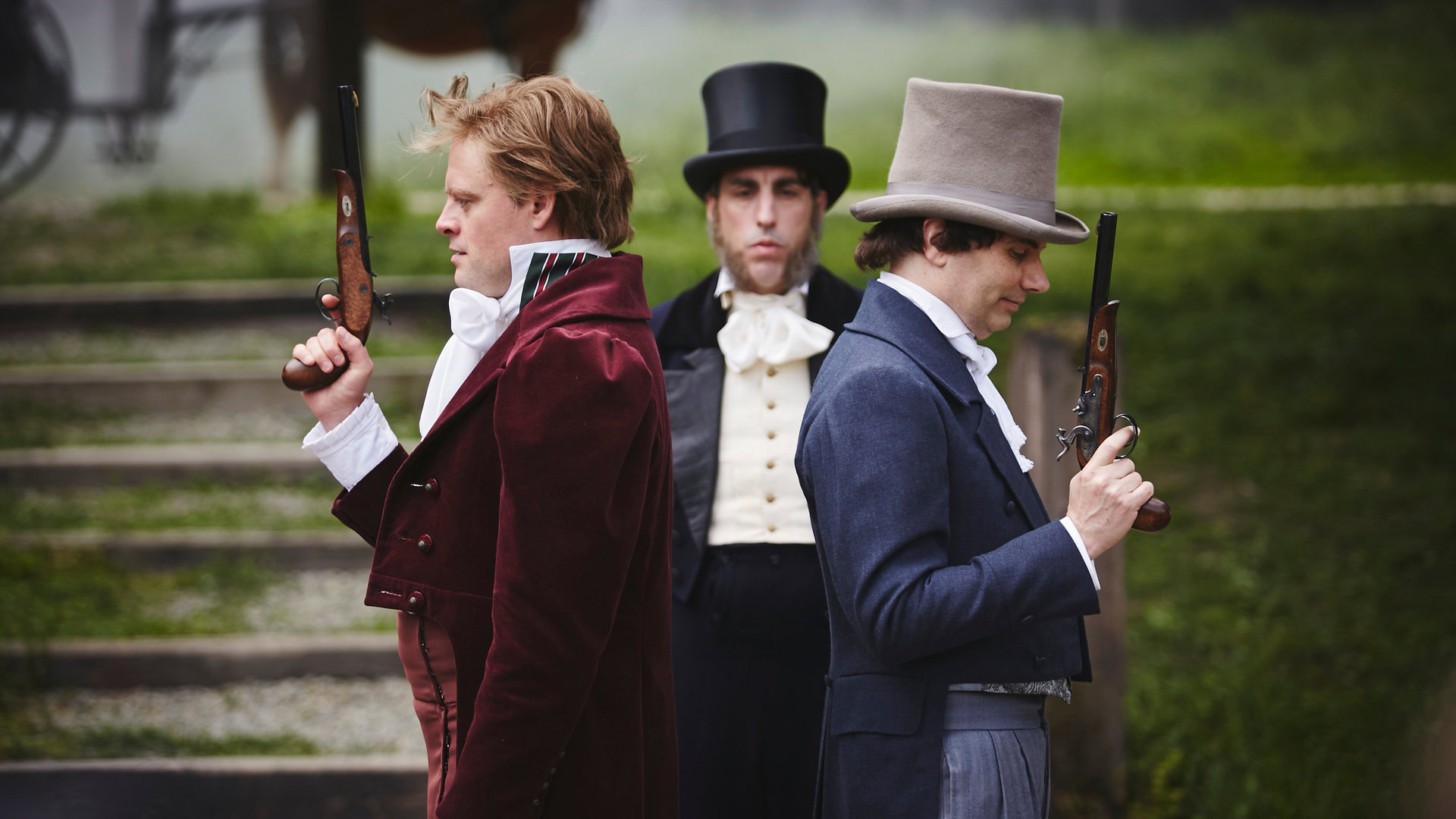 „Sketch History“: Rücken an Rücken stehen zwei Männer mit erhobenen Gewehren (Max Giermann und Carsten Strauch). Beide tragen Anzüge in Rot und Blau. Hinter ihnen steht ein Mann in schwarzem Frack und Zylinder (Alexander Schubert). Er blickt ernst drein.