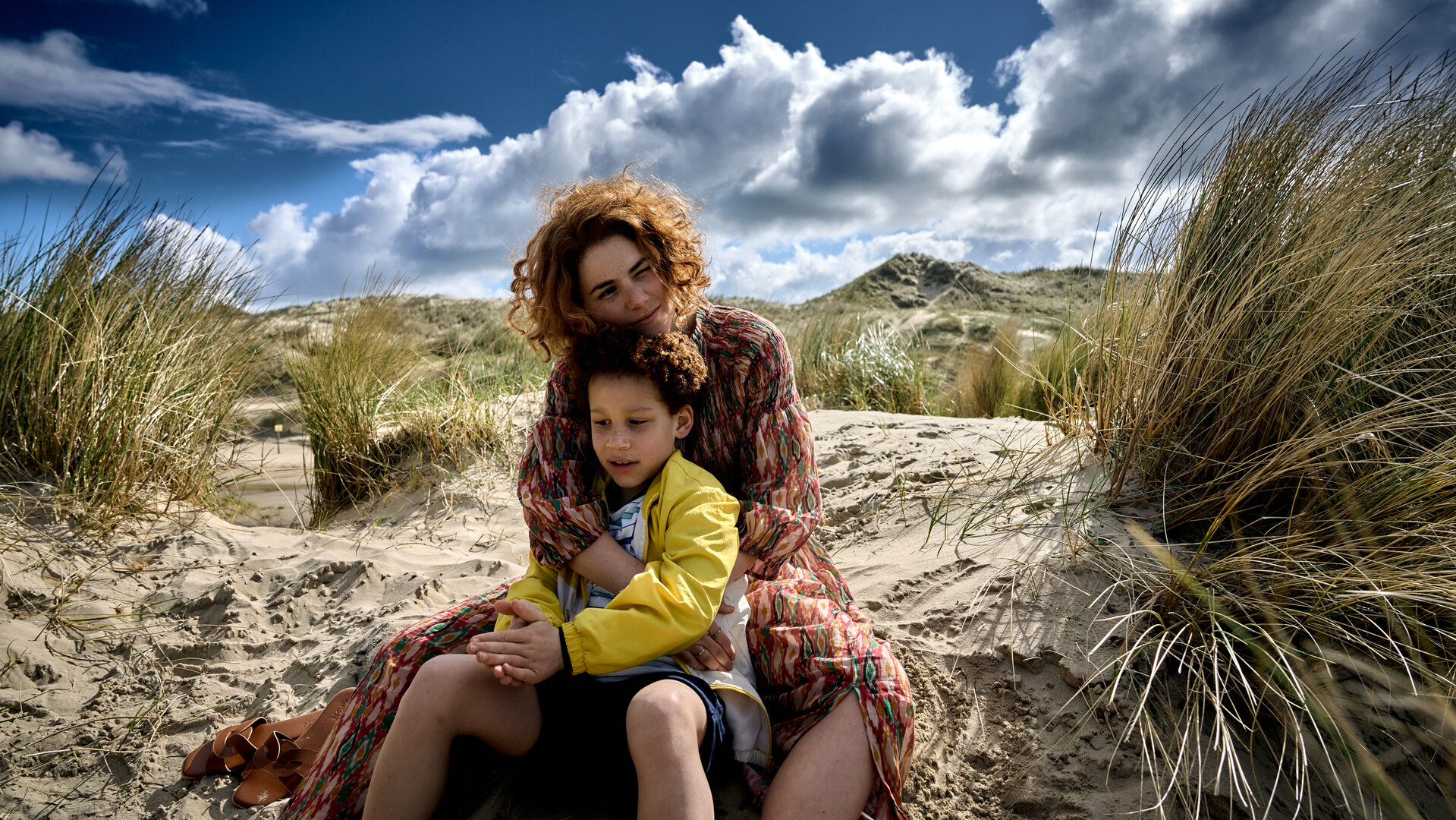 "Don't Fall, Dance - Wer oder was ich bin, ist nicht in diesem Körper": Emma (Hanna van Vliet) und Robin (Joshua Teijema) sitzen am Strand im Sand. Sie hat von hinten ihre Arme um ihn gelegt.