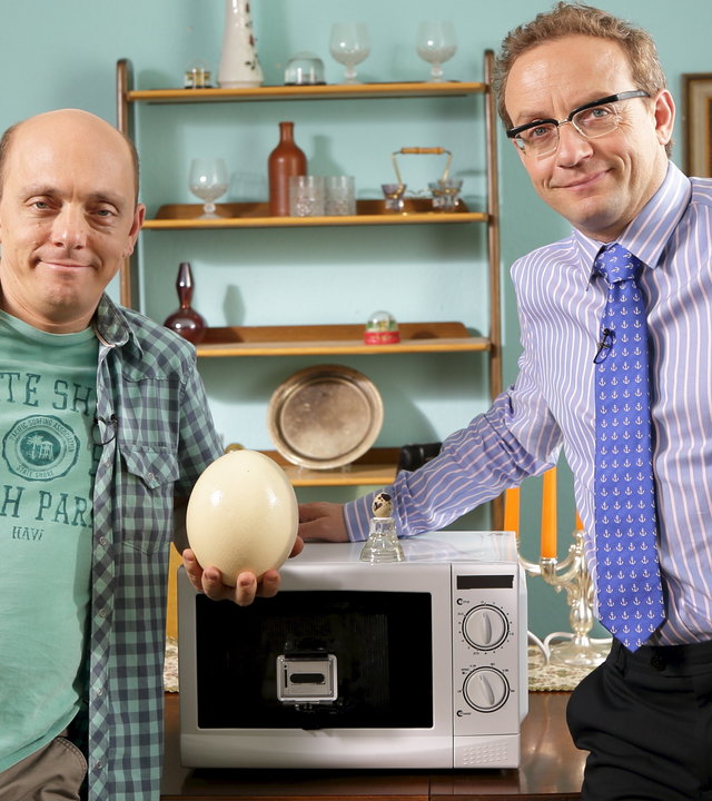 "Nicht Nachmachen": Bernhard Hoëcker und Wigald Boning stehen an einem Tisch, auf dem eine Mikrowelle steht. Beide sehen Richtung Kamera. Bernhard Hoëcker hält ein Straußenei in der Hand.