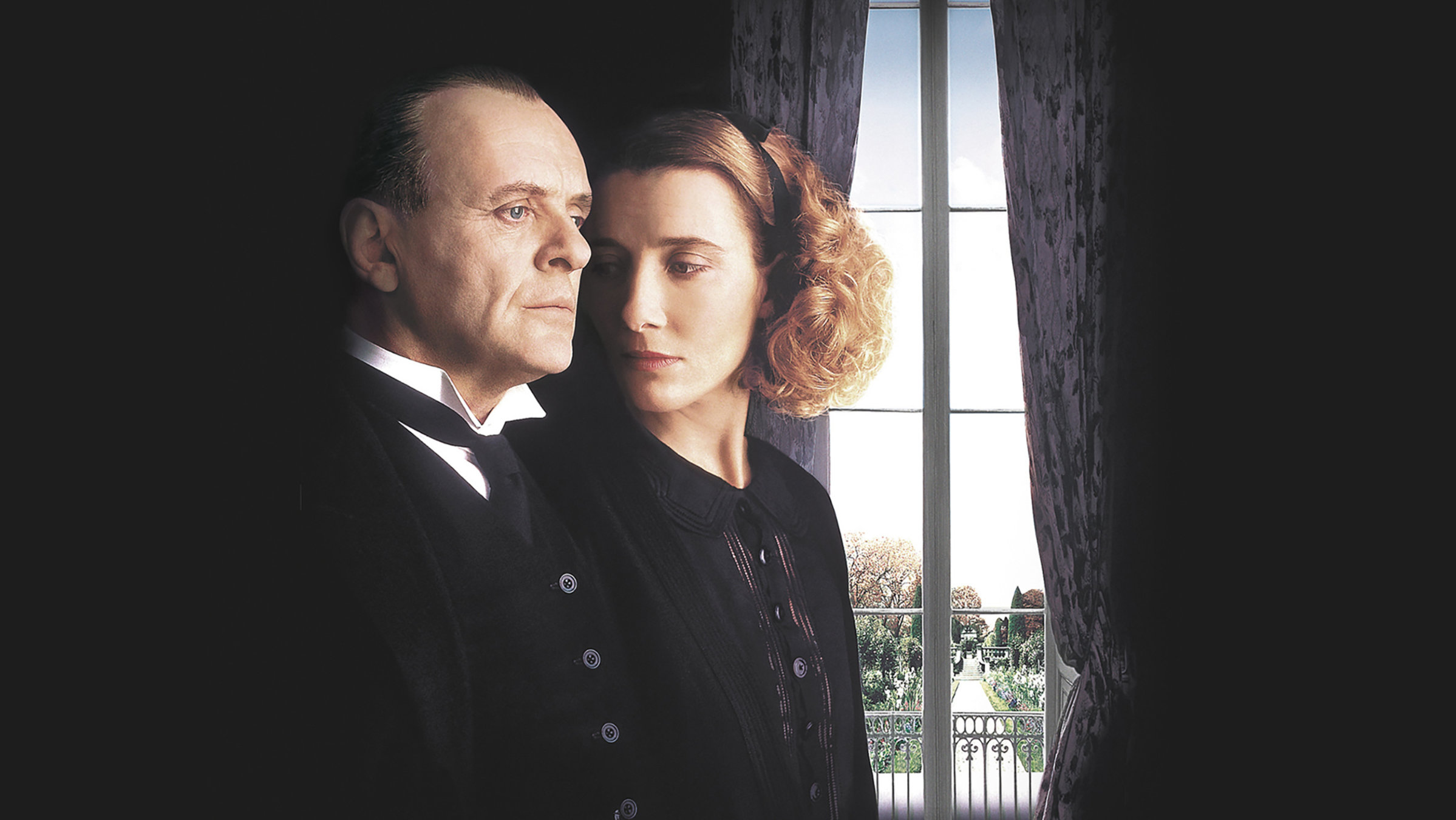 In einem dunklen Zimmer steht der Butler Stevens neben der Haushälterin Miss Kenton. Er schaut mit starrem Blick an ihr vorbei, während sie seitlich auf seine Schulter blickt. Durch einen dunklen Vorhang sieht man durch einen schmalen Spalt nach draußen in eine Art Park.